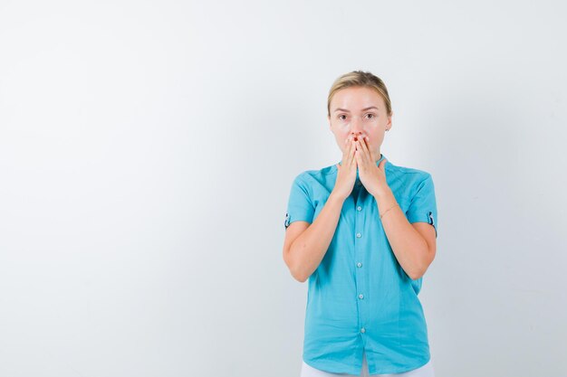 Young female doctor holding hands on mouth in medical uniform, mask and looking puzzled