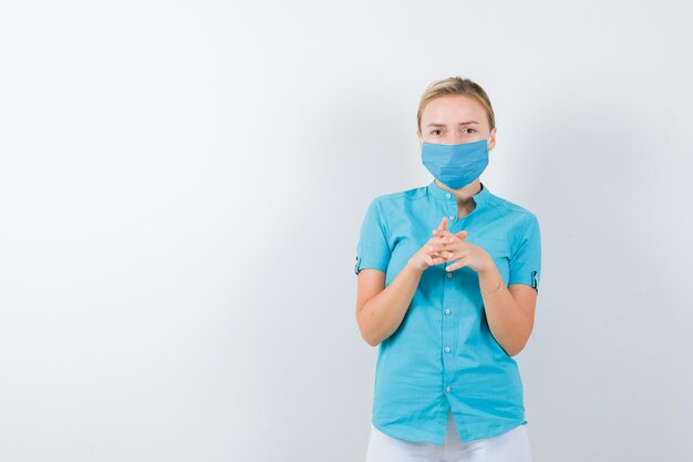 Young female doctor keeping clasped hands near chest in medical uniform