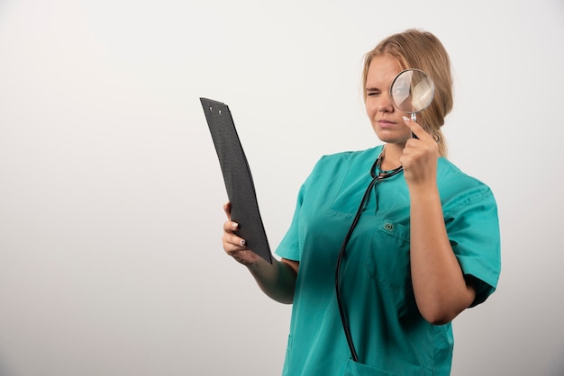 Young female doctor looking through loupe on clipboard . 