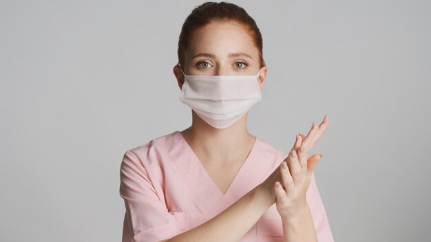 Young female doctor in medical mask washing hands on camera over white background Safety first concept