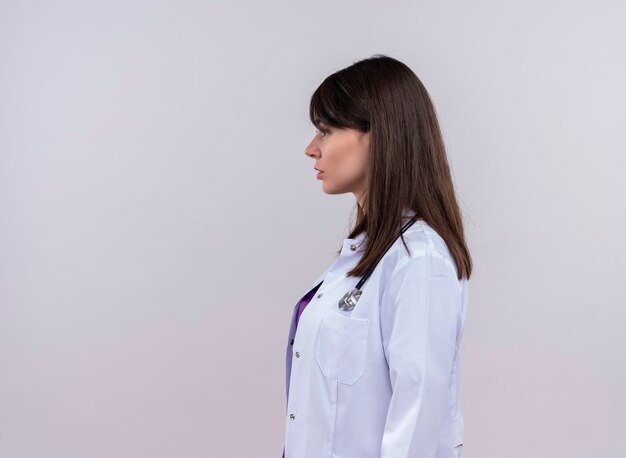 聴診器と医療ローブの若い女性医師は、孤立した白い壁に横に立っています