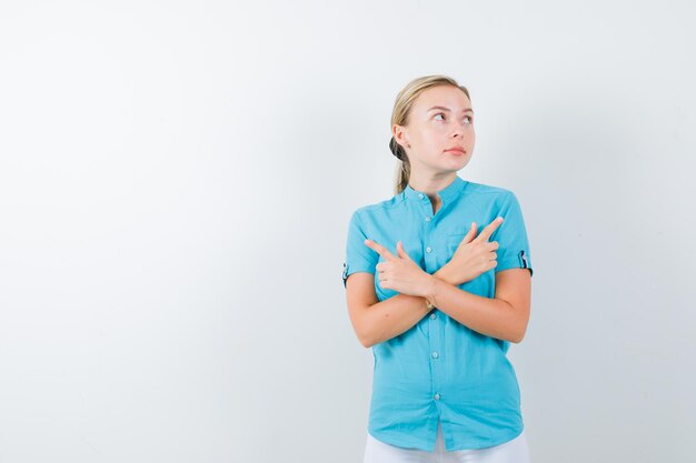 Young female doctor pointing both sides in medical uniform, mask and looking hesitant