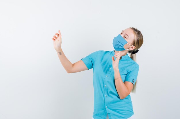 Young female doctor pointing up while closing eyes in uniform and looking peaceful