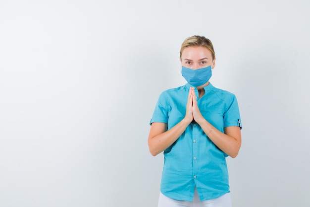 Giovane dottoressa che mostra le mani giunte in un gesto di supplica in uniforme medica