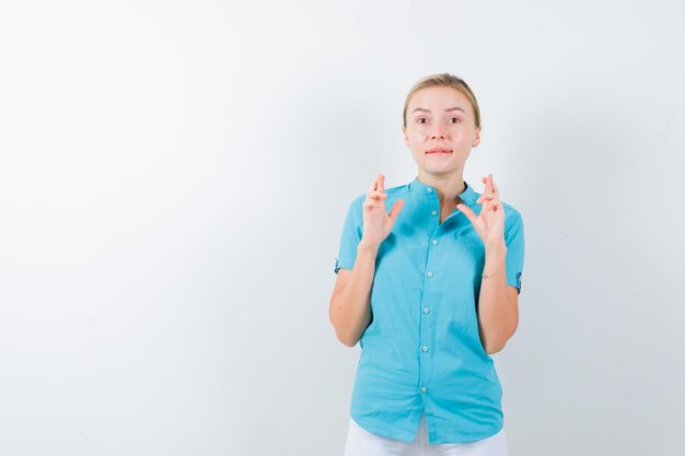 Young female doctor showing crossed fingers in medical uniform, mask and looking hesitant