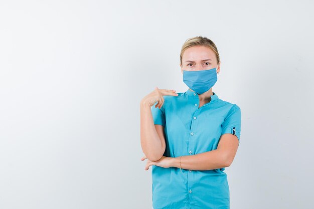 Young female doctor showing gun gesture in uniform and looking serious isolated