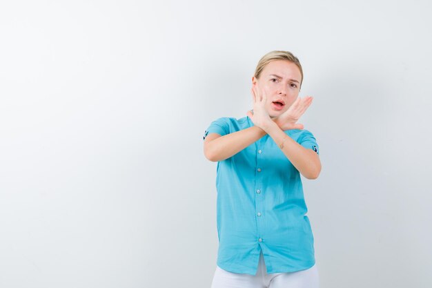 Young female doctor showing stop gesture in medical uniform, mask and looking scared