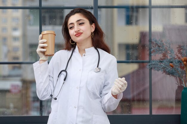 Молодая женщина-врач стоит и пьет кофе Фото высокого качества