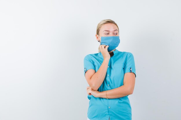 Young female doctor standing in thinking pose in uniform and looking hesitant isolated