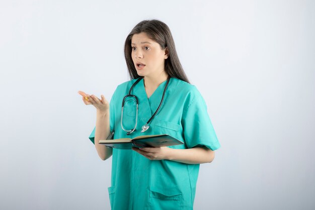 young female doctor standing with notebook and pencil. 