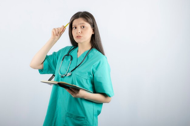 young female doctor standing with notebook and pencil. 