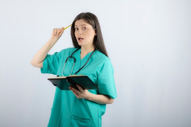 young female doctor standing with notebook and pencil. 