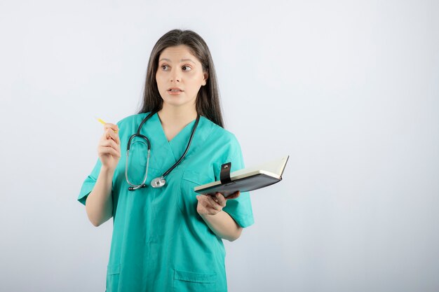 young female doctor standing with notebook and pencil. 