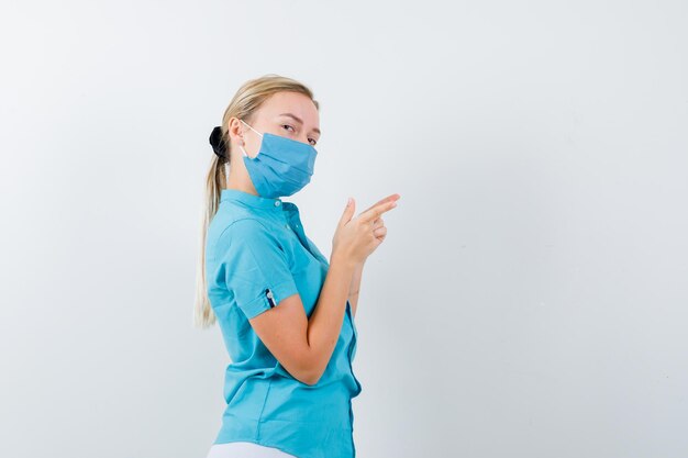 Young female doctor in uniform pointing to the right side and looking confident isolated