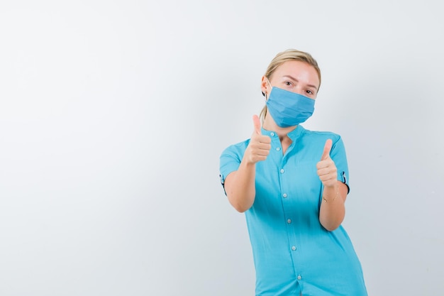 Young female doctor in uniform showing thumbs up and looking confident isolated