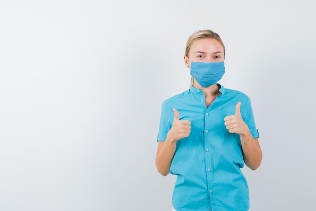 Young female doctor in uniform showing thumbs up and looking happy