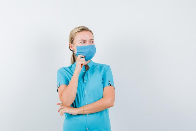 Young female doctor in uniform standing in thinking pose and looking hesitant isolated