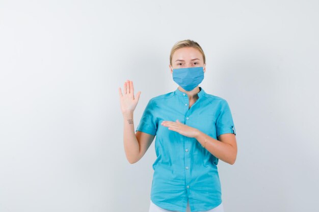 Young female doctor in uniform waving hand for greeting and looking cheery