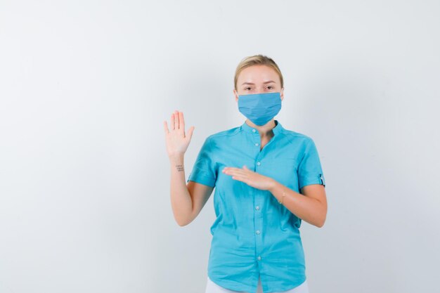 Молодая женщина-врач в форме машет рукой для приветствия и веселого вида