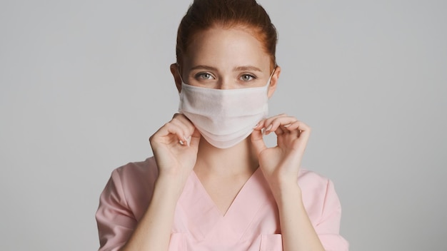 白い背景の上のカメラに医療マスクを身に着けている若い女性医師安全コンセプト