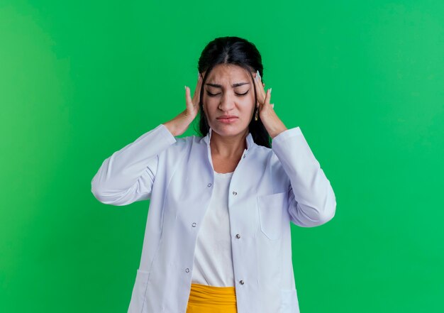 복사 공간 녹색 벽에 고립 된 닫힌 된 눈으로 두통으로 고통을 머리를 들고 의료 가운을 입고 젊은 여성 의사