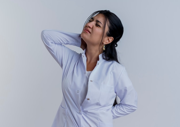 Free photo young female doctor wearing medical robe putting hands behind neck and behind back suffering from pain with closed eyes isolated