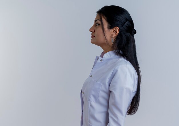 Young female doctor wearing medical robe standing in profile view looking straight isolated