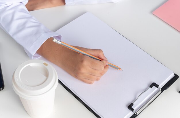 Young female doctor wearing medical robe with stethoscope and glasses sits at table with medical tools - isolated on blue background