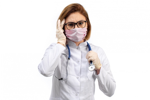 Молодая женщина-врач в белом медицинском костюме со стетоскопом в белой защитной маске на белом