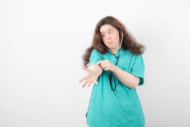 Free photo young female doctor with down syndrome checking her pulse over white wall.