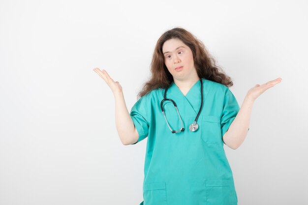 Young female doctor with down syndrome standing on white wall.