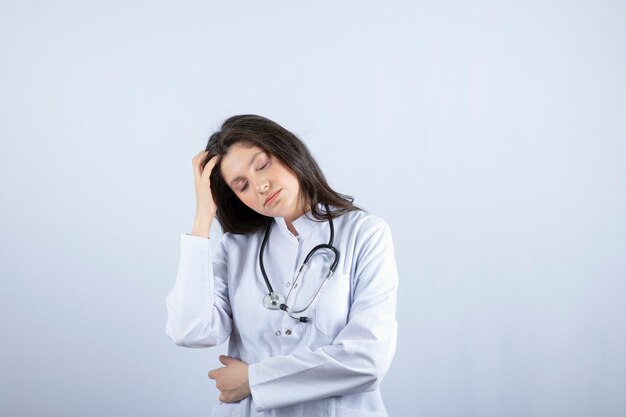 Young female doctor with stethoscope having headache on white wall.