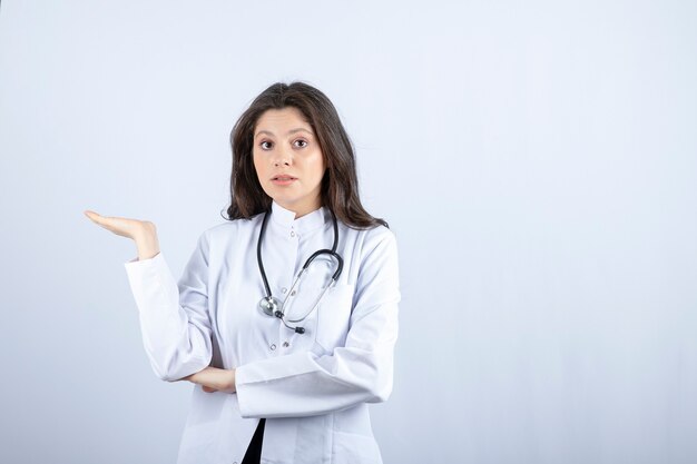 Young female doctor with stethoscope holding copy space on grey. 