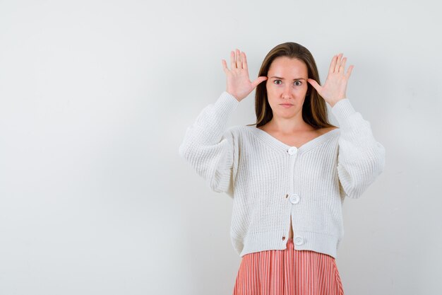 Giovane femmina che fa il gesto delle orecchie in cardigan e gonna che sembrano divertenti isolate