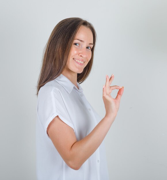 Young female doing ok sign in white shirt and looking pleased