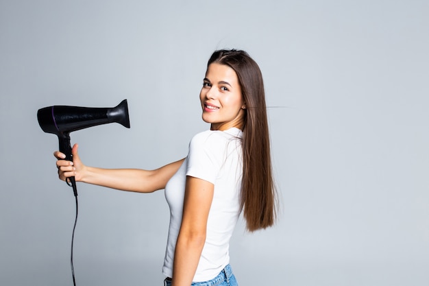 Foto gratuita giovane femmina che asciuga i suoi bei capelli castana con asciugacapelli isolato su bianco