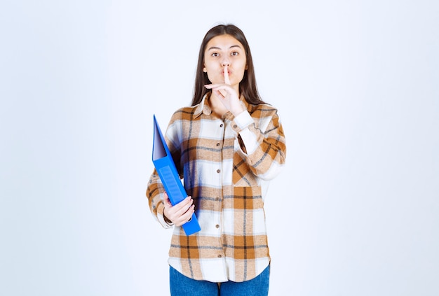 Young female employee holding blue holder and giving silence sign. 