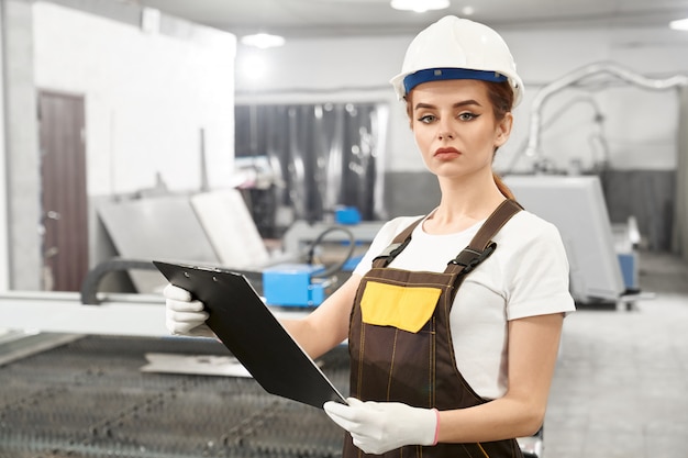 Young female engineer posing while working on metal factory