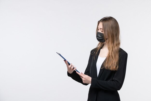 Молодая женщина-предприниматель в костюме в медицинской маске и глядя на документы на белой стене