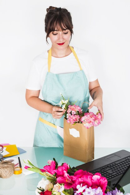Молодая женщина-флорист, упорядочивая цветы в бумажный пакет за столом