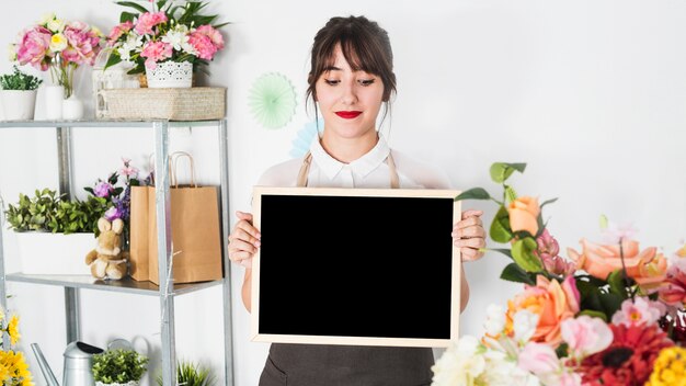 Young female florist holding blank slate in floral shop