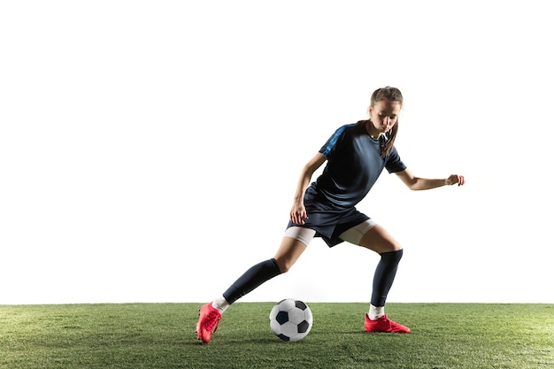 Young female football or soccer player with long hair in sportwear and boots kicking ball for the goal in jump isolated on white background. Concept of healthy lifestyle, professional sport, hobby.