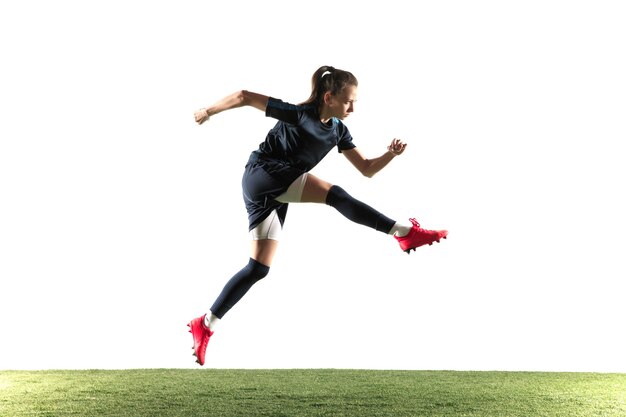 スポーツウェアとブーツで長い髪の若い女性のサッカー選手またはサッカー選手は、白い背景で隔離のジャンプでゴールのためにボールを蹴ります。健康的なライフスタイル、プロスポーツ、趣味の概念。