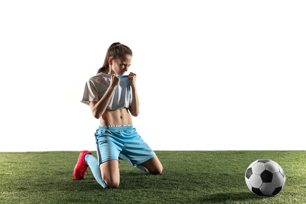 Young female football or soccer player with long hair in sportwear and boots sitting with the ball isolated on white background. Concept of healthy lifestyle, professional sport, hobby.