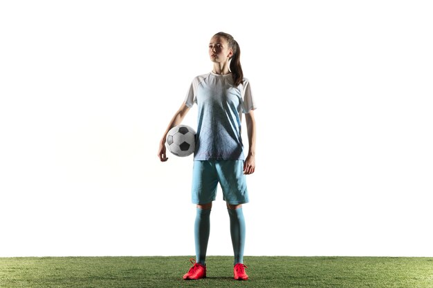 Young female football or soccer player with long hair in sportwear and boots standing with the ball isolated on white background. Concept of healthy lifestyle, professional sport, hobby.