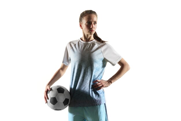 Young female football or soccer player with long hair in sportwear and boots standing with the ball isolated on white background. Concept of healthy lifestyle, professional sport, hobby.