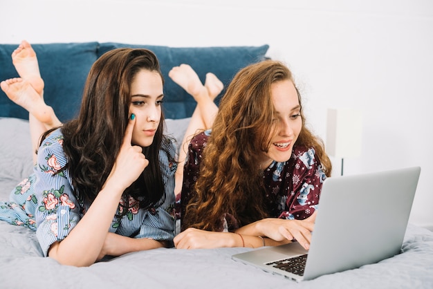 Young female friend lying on bed using laptop