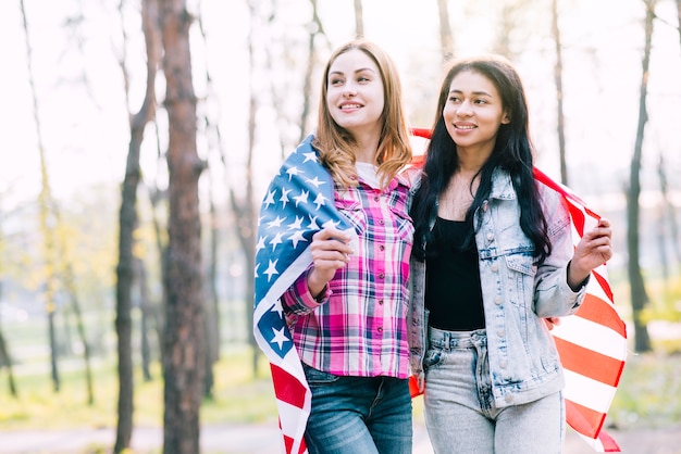 Young female friends wrapping in American flag 