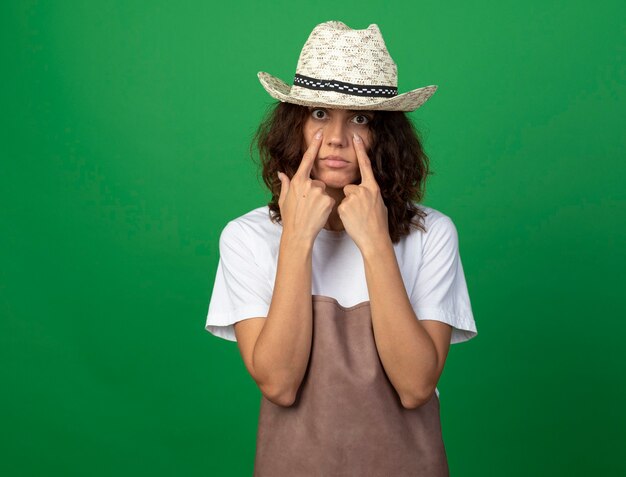 young female gardener in uniform wearing gardening hat pulling down eye lids