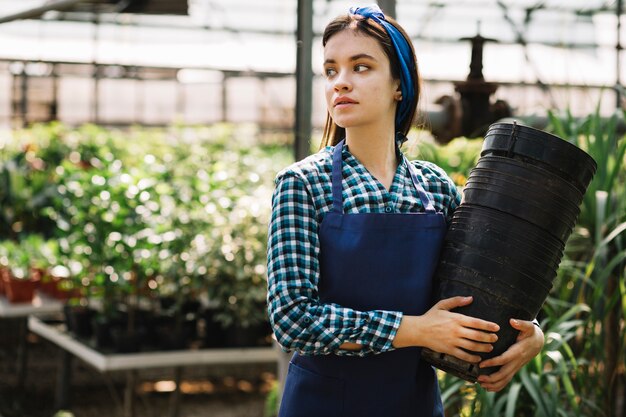 Young female gardener with empty flower pots in greenhouse